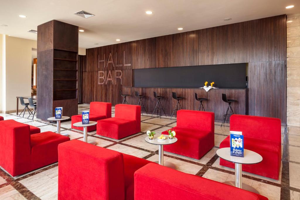 Mūsdienīgs bārs ar sarkaniem krēsliem un elegantiem galdiem, kas piedāvā patīkamu atpūtas vietu. Interjerā ir izmantoti dabīgi materiāli un siltas krāsas, radot viesmīlīgu atmosfēru.