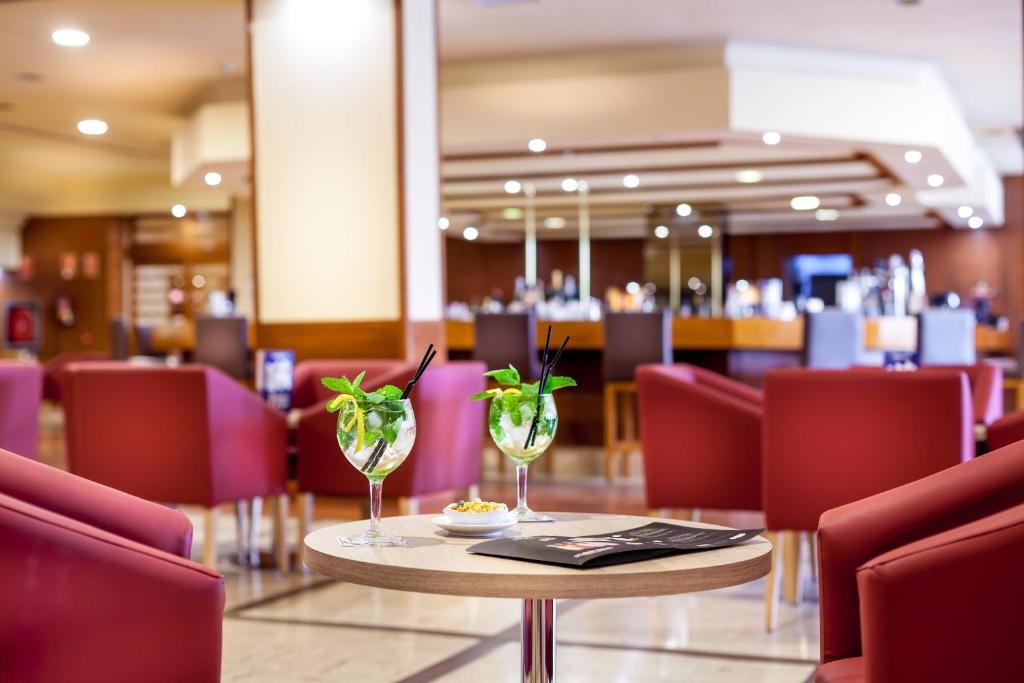 Skaisti kokteiļi ar piparmētru un citronu sēž uz galda kafejnīcā, kurā redzami sarkani krēsli un bārs fona. Ideāla vide relaksācijai un baudīšanai.
