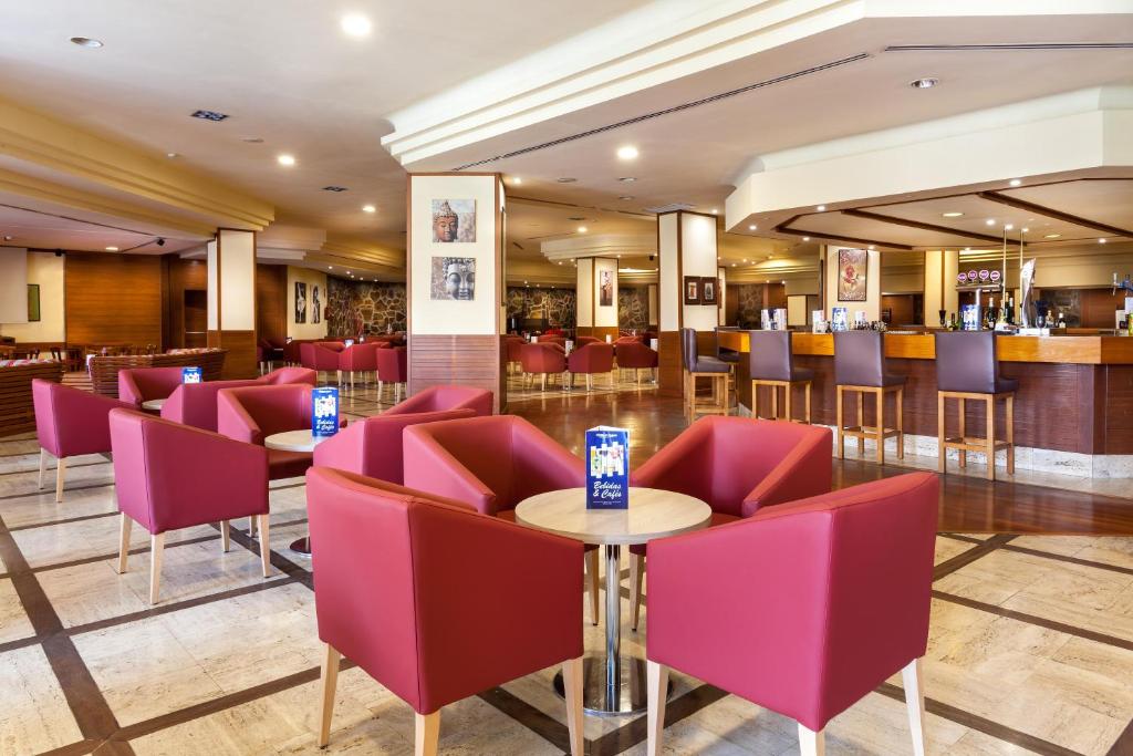 Mūsdienīgs bārs ar sarkaniem krēsliem un koka galdu, kas rada viesmīlīgu atmosfēru. Interjerā ir eleganti apgaismojumi un mākslas darbi uz sienām.