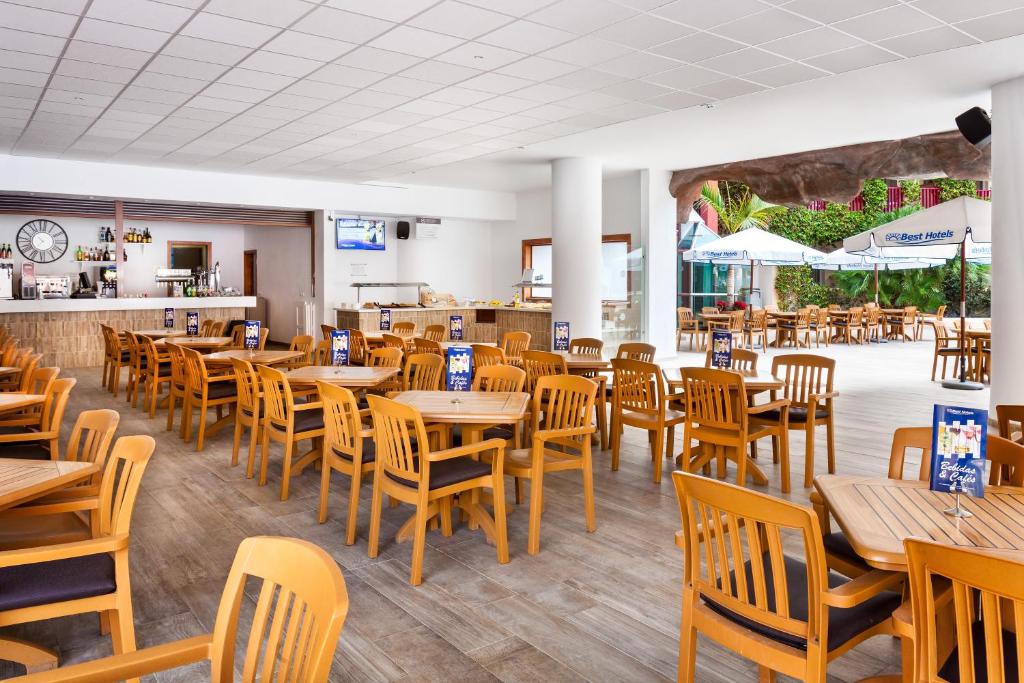 Kafejnīca ar koka galdiem un krēsliem, plaša telpa ar bāru un piekļuvi āra terasei. Gaisīga atmosfēra ar skatu uz dārzu.