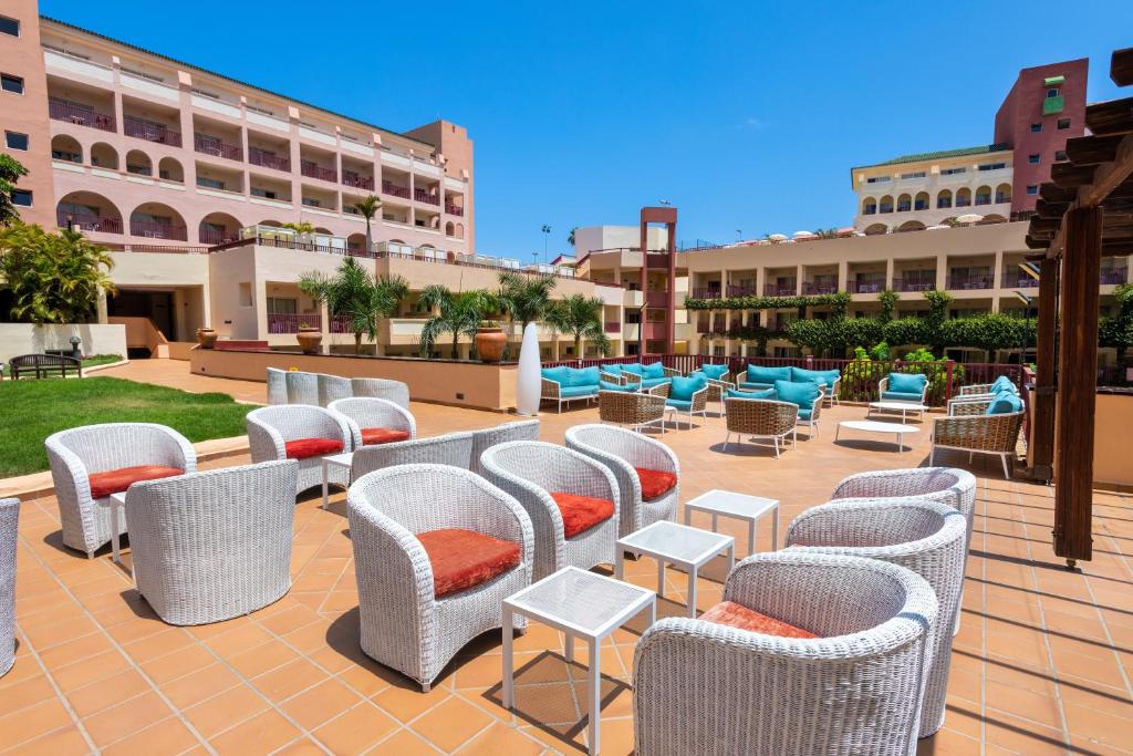 Mūsdienīgs viesnīcas terases dizains ar baltām vītņu krēslām un zilo spilvenu sēdvietām, kas aicina atpūsties saulainā dienā. Terase ir ieskauta zaļumiem un sniedz lielisku skatu uz viesnīcas ēku.