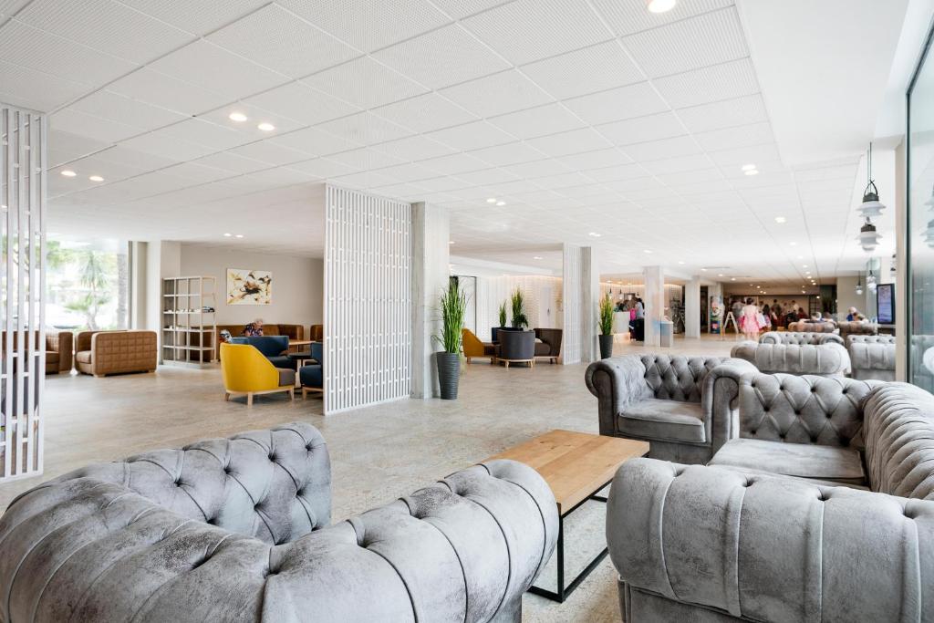 Mūsdienīgs viesnīcas vestibils ar elegantiem dīvāniem un koka galdu, kurā apmeklētāji var relaksēties. Gaismas un zaļumi piešķir telpai patīkamu atmosfēru.