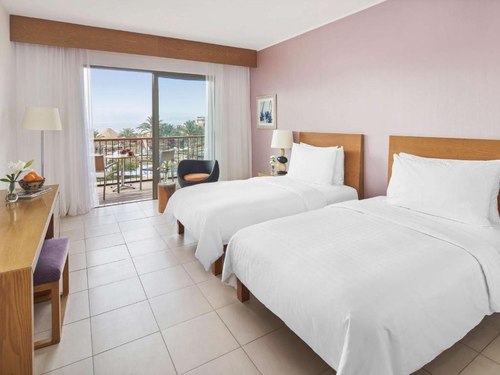 Mūsdienīgs viesnīcas numurs ar divām atsevišķām gultām, gaišām sienām un lielu logu, caur kuru redzams skats uz ārpusi. Numurā ir koka mēbeles un gaismas dekorācijas, radot patīkamu atmosfēru.