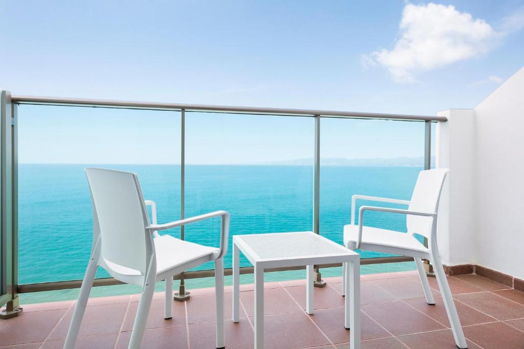 Balcony with ocean view featuring white chairs and a small table, perfect for relaxing and enjoying the scenery.