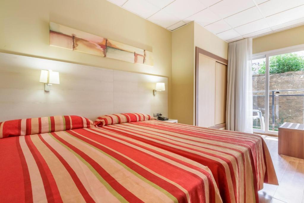 Mūsdienīgs viesnīcas numurs ar divām gultām un sarkaniem svītrainiem gultasveļām, apgaismots ar siltu gaismu un logu, kas ved uz ārpusi.