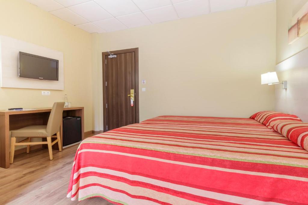 Mūsdienīga viesnīcas istaba ar divguļamo gultu, koka grīdu un rakstāmgaldu. Uz sienas ir televizors, blakus ir ledusskapis un durvis uz koridoru.