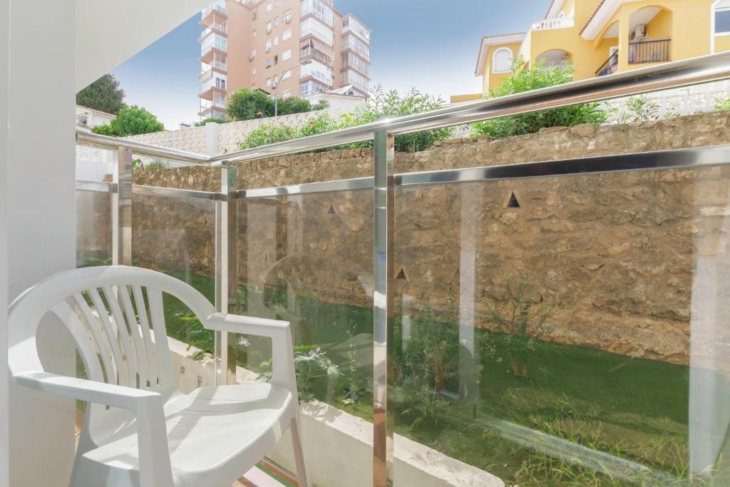 Balkons ar baltu plastmasas krēslu un skatu uz dārzu, kur redzama akmens siena un zaļumi. Ideāls atpūtai un relaksācijai.