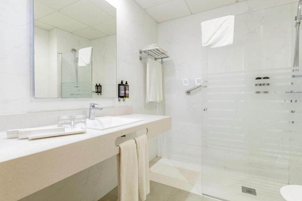 Mūsdienīga vannas istaba ar elegantu izskatu, iekļaujot stikla dušu, lielu spoguli un tīru, balto izskatu. Vannas istabā ir arī higiēnas piederumi un dvieļi, kas nodrošina komfortu.