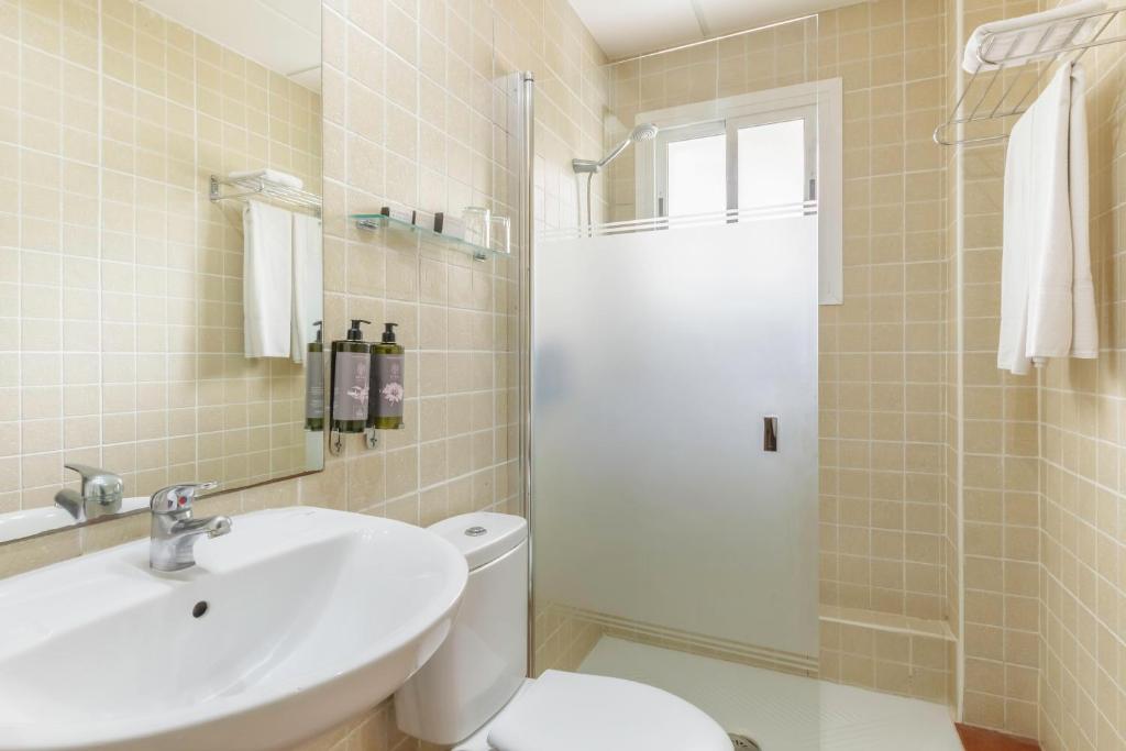 Mūsdienīgs vannas istabas interjers ar dušu, izlietni un spoguli, kurā redzami higiēnas līdzekļi un dvieļi. Sienas ir klātas ar gaišām flīzēm, radot patīkamu atmosfēru.