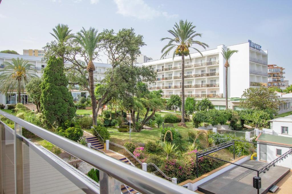 Zaļš viesnīcas dārzs ar palmām un krūmiem, blakus baltiem viesnīcu ēkām. Ideāla vieta atpūtai un relaksācijai.