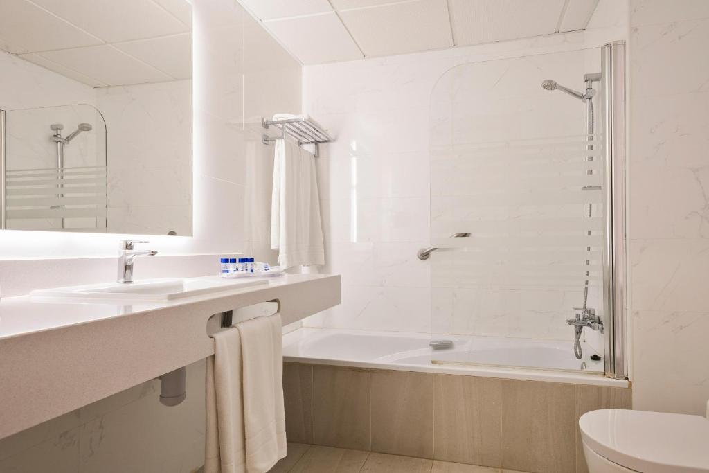 Mūsdienīgs vannas istabas interjers ar vannu, dušu un izsmalcinātu apgaismojumu. Uz galda izvietoti higiēnas piederumi un dvieļi.