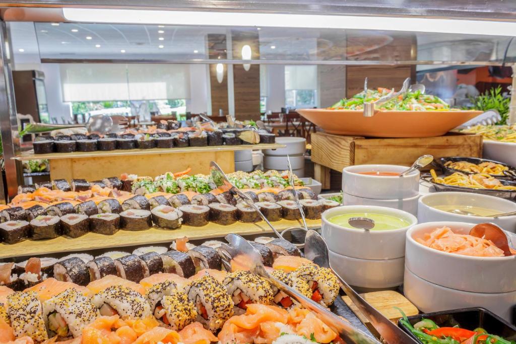 Svaigu suši un salātu bufete ar dažādām piedevām un mērču traukiem, kas izkārtoti uz koka plauktiem.