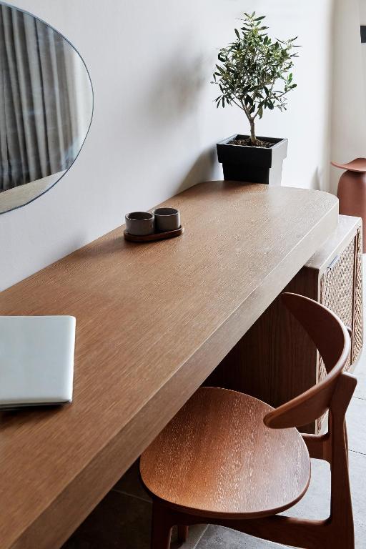 Moderns interjers ar koka galdu, ērtu krēslu un dekoratīvu augu. Uz galda redzams klēpjdators un divas krūzītes.