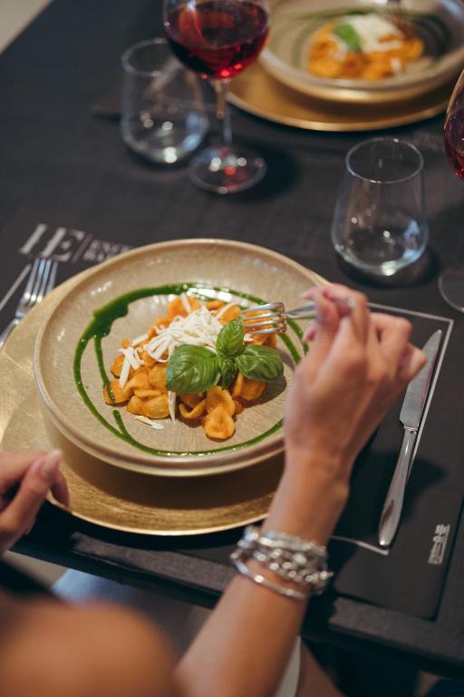 Gatavošanās brīnišķīgai maltītei ar makaronu ēdienu, dekorētu ar baziliku un zaļo mērci, pie galda ar sarkanvīnu un elegantiem traukiem.