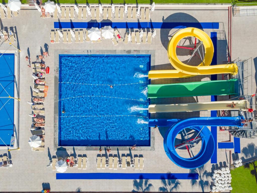 Baseins ar krāsainiem ūdens slidkalniņiem un atpūtas zonu, kurā cilvēki baudīja sauli. Ap ūdeni ir sauļošanās krēsli un saulessargi.