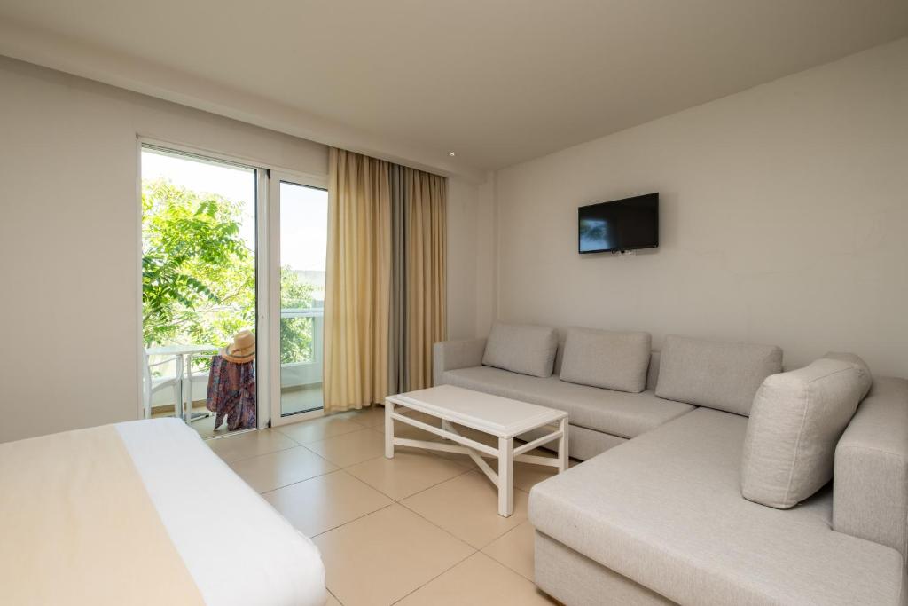 Mūsdienīgs viesnīcas numurs ar gaišiem toņiem, ērtu dīvānu un nelielu galdiņu. Logi vērsti uz zaļu dārzu, radot patīkamu atmosfēru.