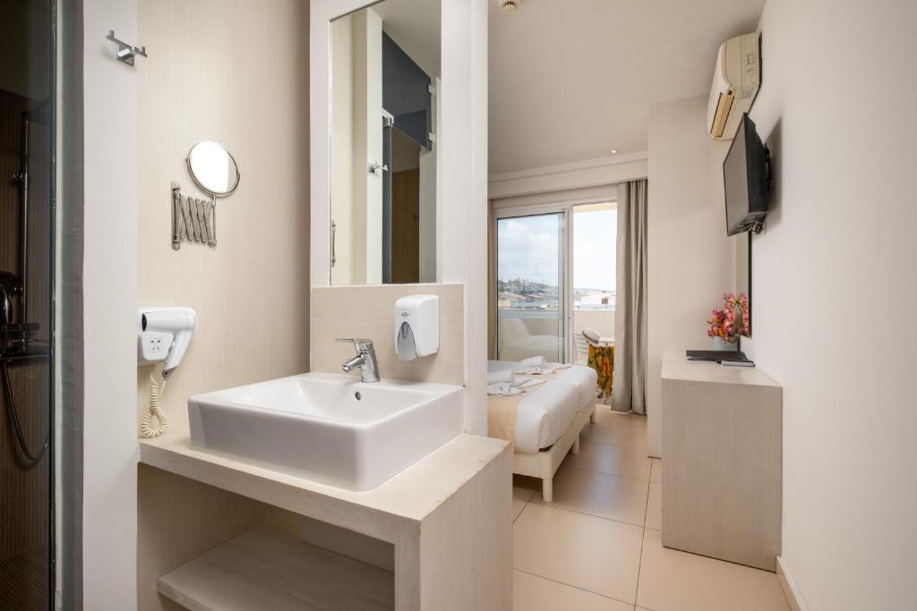 Mūsdienīgs viesnīcas numura interjers ar vannas istabu, kas ietver izlietni, spoguli un matu žāvētāju. Logu paveras skats uz ārpusi, bet telpā ir televizors un gulta.