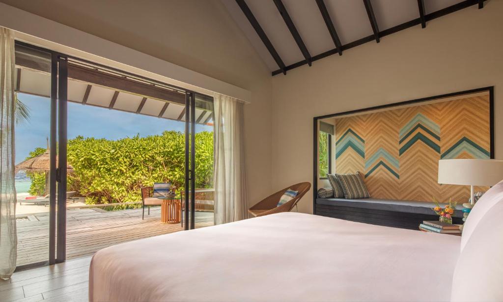 Mūsdienīgs guļamistabas interjers ar plašām durvīm, kas ved uz āra terasi, un skatu uz dabu. Telpā ir eleganta apdare ar krāsainu sienu mākslu un komfortablu mēbelējumu.