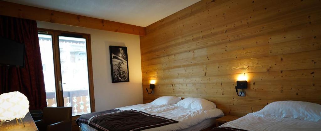 Mūsdienīga viesnīcas numura iekārtojums ar koka sienām, divām gultām un lieliem logiem, caur kuriem redzama ārpuse. Numurā ir televizors un siltas gaismas apgaismojums.