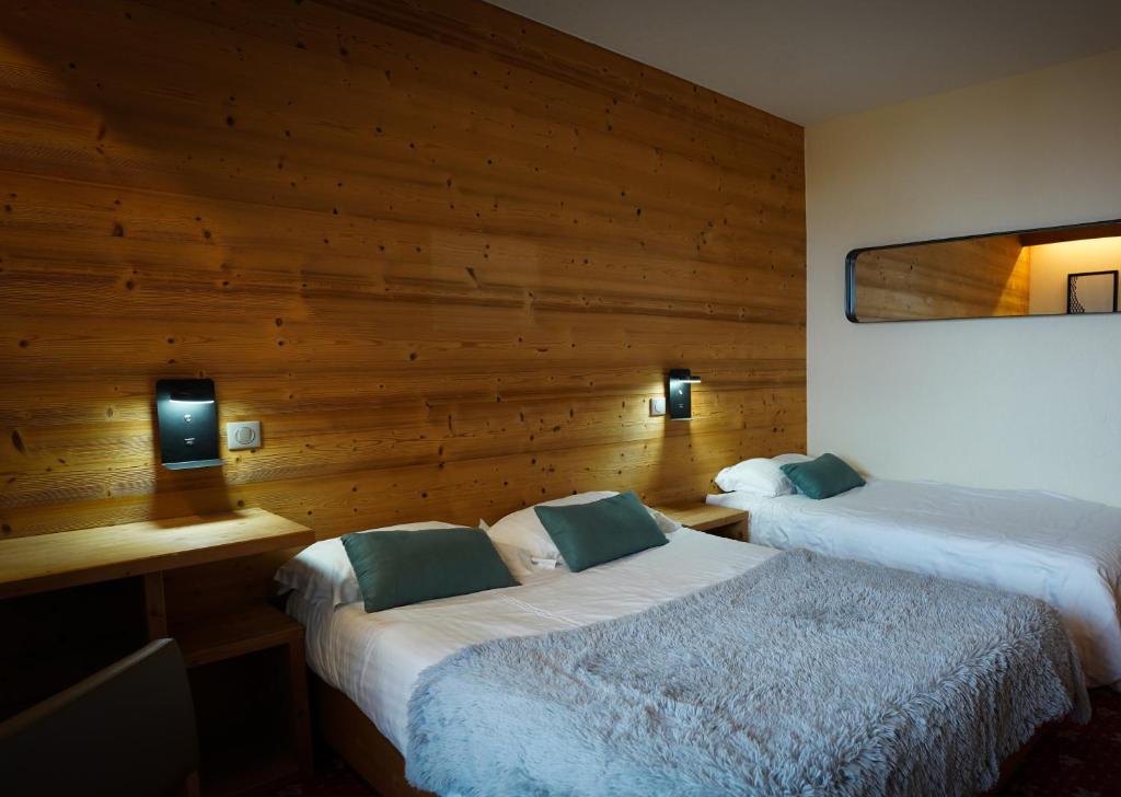 Mūsdienīgs viesnīcas numurs ar divām gultām, gaišām krāsām un koka sienu, kas rada siltu atmosfēru. Numurā ir galda lampas un spogulis.