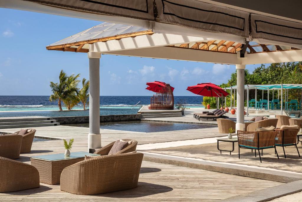 Tropu kūrorta terase ar skatu uz okeānu, kur redzami ērti krēsli, peldbaseins un sarkani saules aizsargi. Ideāla vieta relaksācijai un atpūtai.