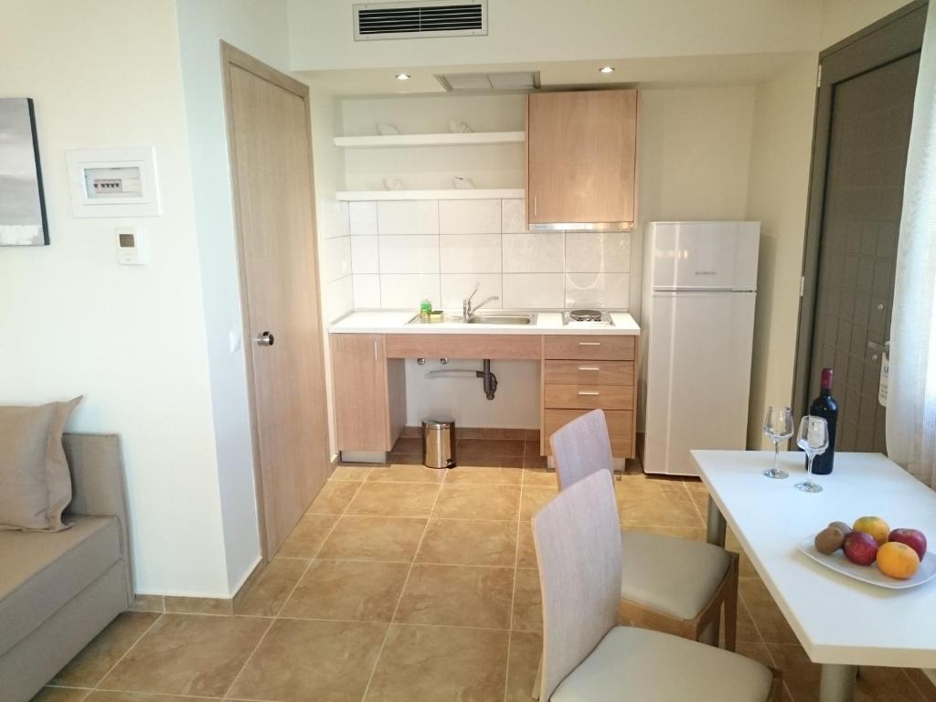 Mūsdienīga virtuve ar koka mēbelēm, balto ledusskapi un ēdamgaldu, uz kura atrodas augļi un vīns. Telpa ir gaiša un sakārtota, ar komfortablu dīvānu blakus.