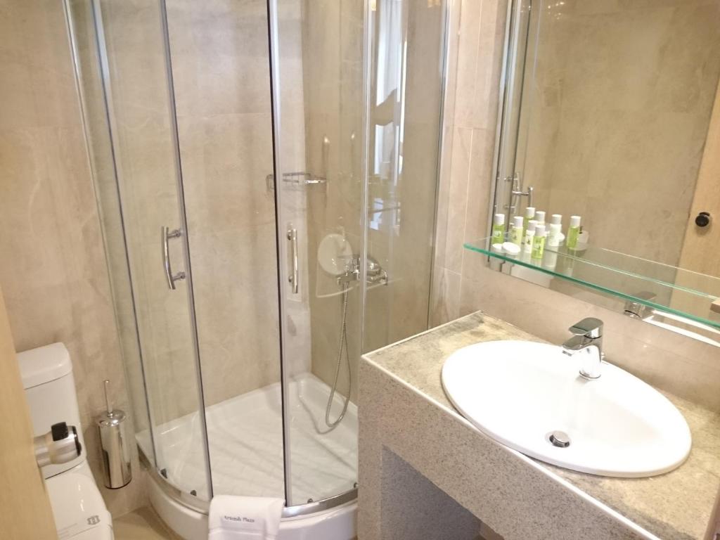 Mūsdienīgs vannas istabas iekārtojums ar stikla dušu, izsmalcinātu izlietni un higiēnas piederumiem uz plaukta. Ideāla vieta relaksācijai un atpūtai.