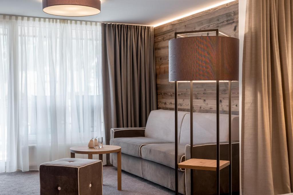 Mūsdienīgs viesnīcas numurs ar pelēku dīvānu, koka apdari un elegantu lampu. Interjers ir gaišs un patīkams, radot mājīgu atmosfēru.