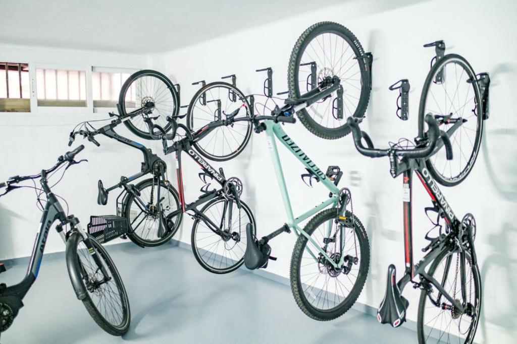 Velosipēdu stends ar vairākām piekārtām riepām, kas uzstādīts gaišā telpā ar logiem. Ideāls risinājums velosipēdu glabāšanai.