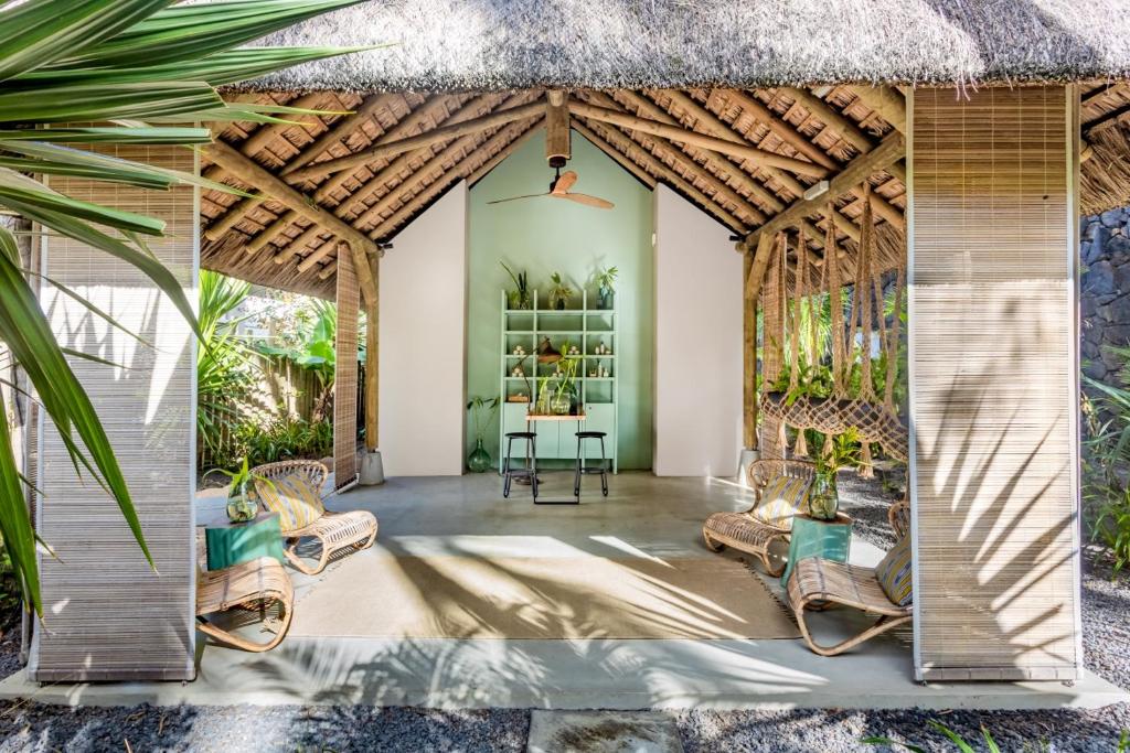 Atklāta telpa ar jumtu no salmiem, kas ietver dabīgu apdari un ērtas sēdvietas. Interjers ir piepildīts ar zaļumiem un modernu dizainu, radot relaksējošu atmosfēru.