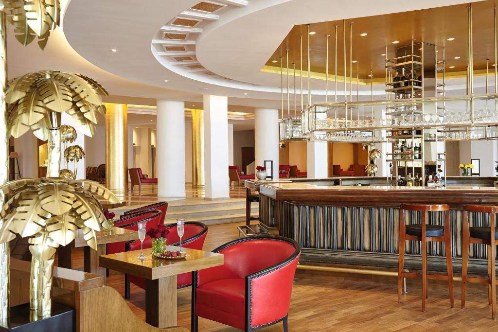 Elegants bārs ar mūsdienīgu interjeru, sarkaniem krēsliem un zeltainiem dekoratīviem elementiem, kas rada greznu atmosfēru. Ideāla vieta relaksācijai un atpūtai.