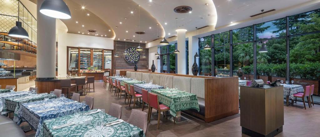 Mūsdienīgs restorāns ar elegantām galdiem un krēslu izkārtojumu, kas piedāvā plašu skatu uz dārzu. Interjers apvieno modernus un tradicionālus elementus, radot patīkamu atmosfēru.