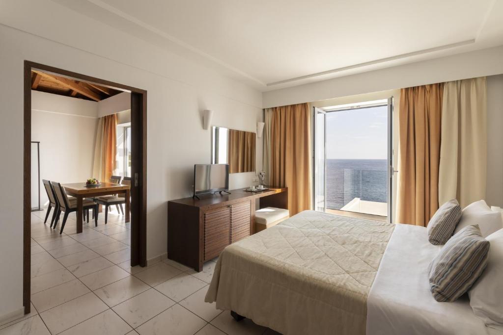 Mūsdienīga viesnīcas numura interjers ar skatu uz jūru, kurā redzama guļamistaba un atsevišķa ēdamzona. Gaismas toņi un plašums rada patīkamu atmosfēru.