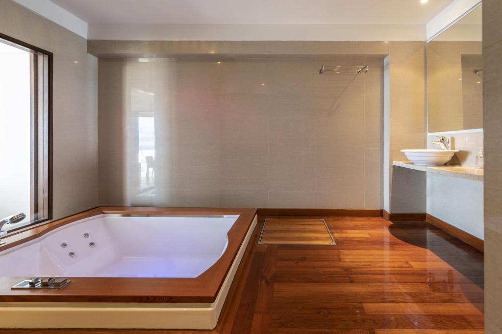 Mūsdienīgs vannas istabas interjers ar džakuzi un elegantu koka grīdu, radot relaksējošu atmosfēru. Gaismas un telpu plānojums piešķir telpai plašuma sajūtu.