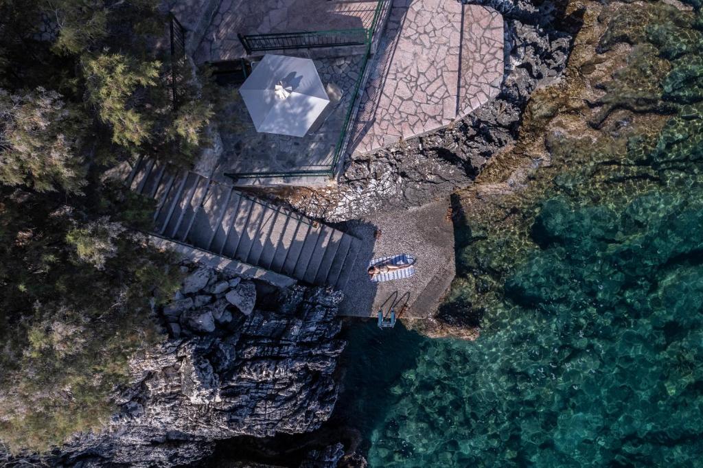 Pārsedzēta terase pie ūdens, kur cilvēki atpūšas uz pludmales gultām, apņem akmeņaini krasts un skaidrs ūdens. Ideāla vieta relaksācijai un saules baudīšanai.