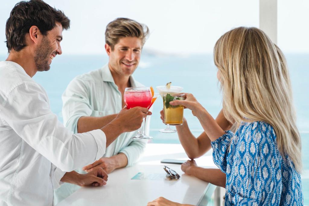 Cilvēki svin kopā, paceldami kokteiļus pie pludmales bāra, ar skatu uz jūru.