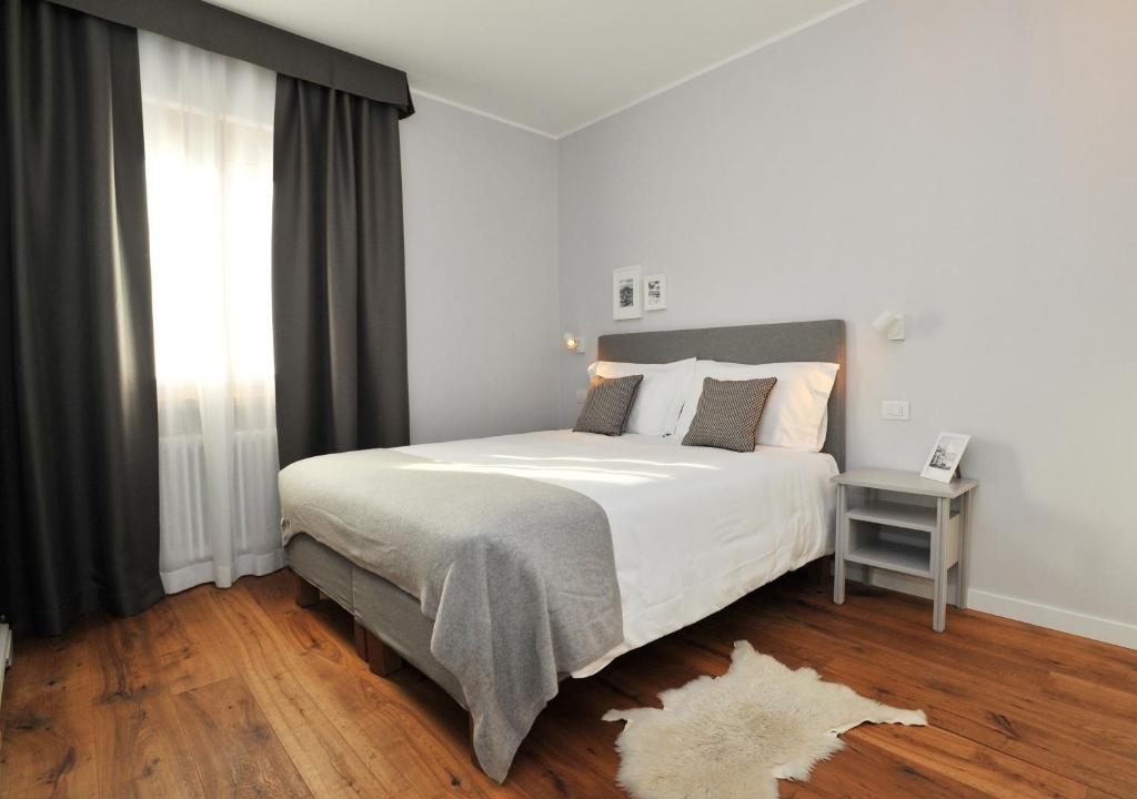 Mūsdienīgs guļamistabas interjers ar ērtu gultu, greznām spilveniem un minimālistisku dizainu. Logi ar tumšām aizkariem ļauj gaismai ieplūst, radot patīkamu atmosfēru.