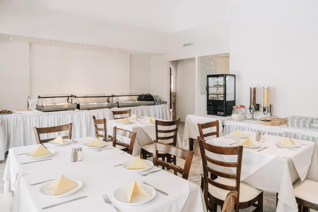 Gaiša un moderna restorāna iekšiene ar ēdamgaldiem, uz kuriem ir šķīvji ar salocītām salvetēm. Fons ietver bufetes staciju un dzērienu automātu.