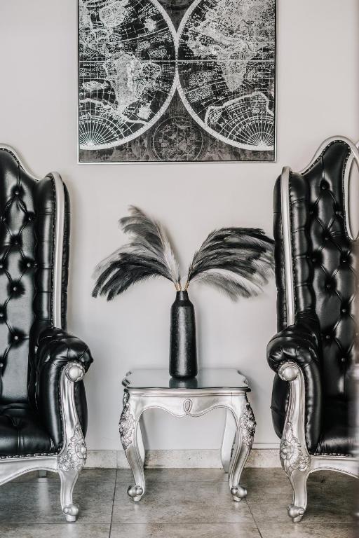 Elegants interjers ar melnām ādas krēslām un sudraba galdiņu, uz kura atrodas melna vāze ar dekoratīvām lapām. Sienā redzama pasaules kartes ilustrācija.