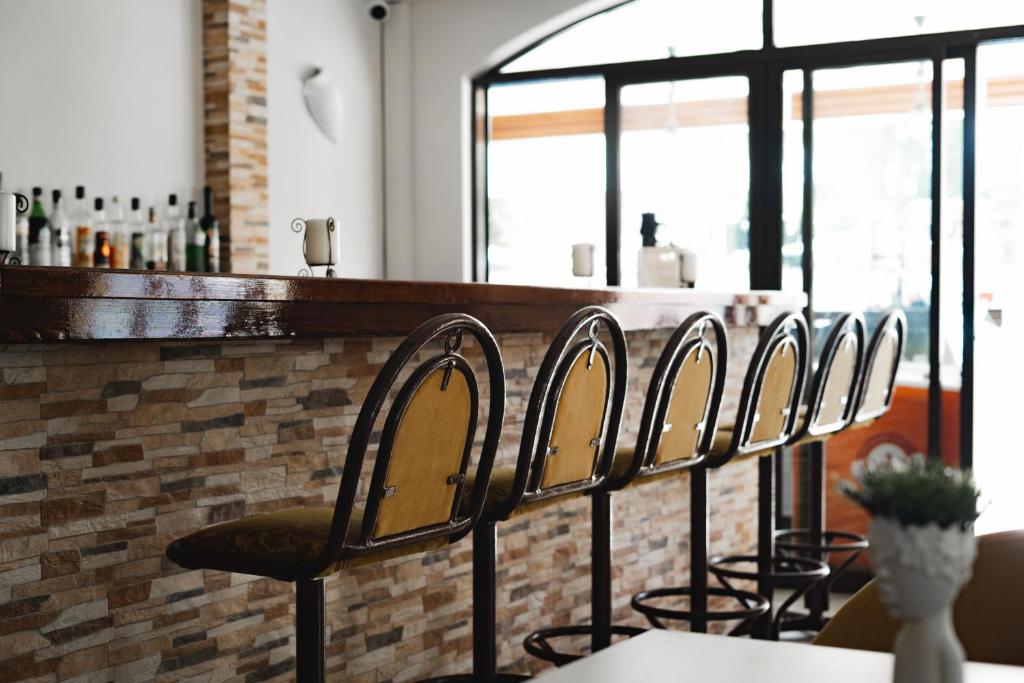 Kafejnīcas bārs ar stilīgiem krēsliem un koka darba virsmu, kas atrodas pie liela loga, caur kuru ieplūst dabiskais apgaismojums.