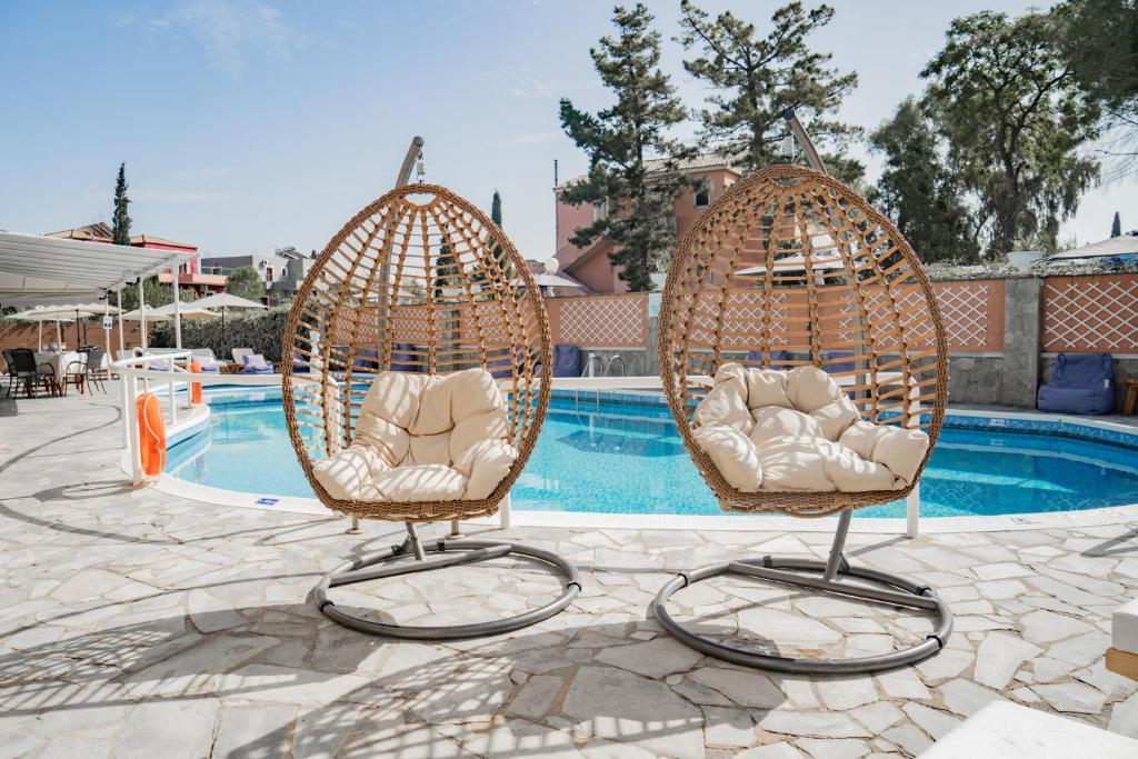 Peldbaseina zona ar divām stilīgām šūpuļkrēslām, kuras ir izgatavotas no rotangpalmas un nodrošina komfortu un relaksāciju. Apkārt ir zaļi koki un saulains laiks.