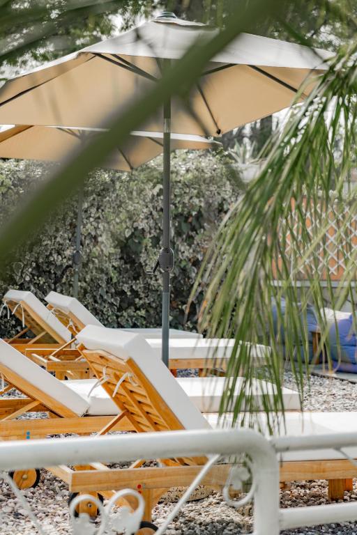 Saulainā atpūtas zona ar koka sauļošanās krēsliem un lieliem lietussargiem, ieskauta zaļiem augiem un akmeņiem. Ideāla vieta relaksācijai un atpūtai.