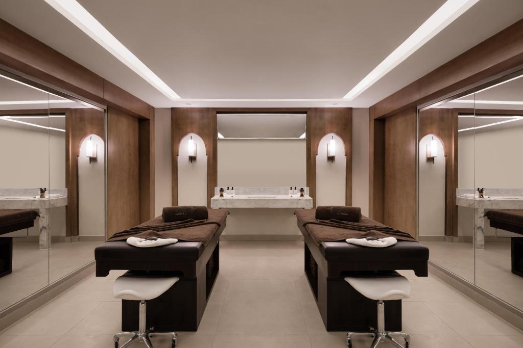 Mūsdienīgs spa telpa ar divām masāžas galdiem, elegantām spoguļa sienām un gaismas elementiem, radot relaksējošu atmosfēru. Komforts un estētika apvienojas harmoniskā dizainā.