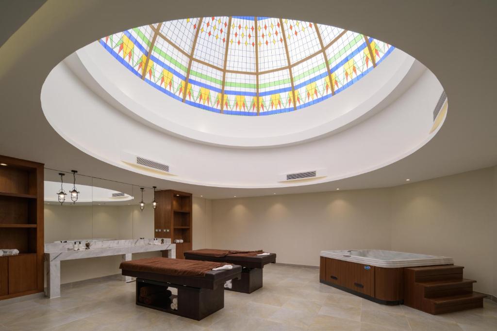 Mūsdienīgs spa interjers ar apgaismotu vitrāžu jumtu, masāžas galdiem un relaksācijas zonu. Eleganta un mierīga atmosfēra, kas aicina uz atpūtu.