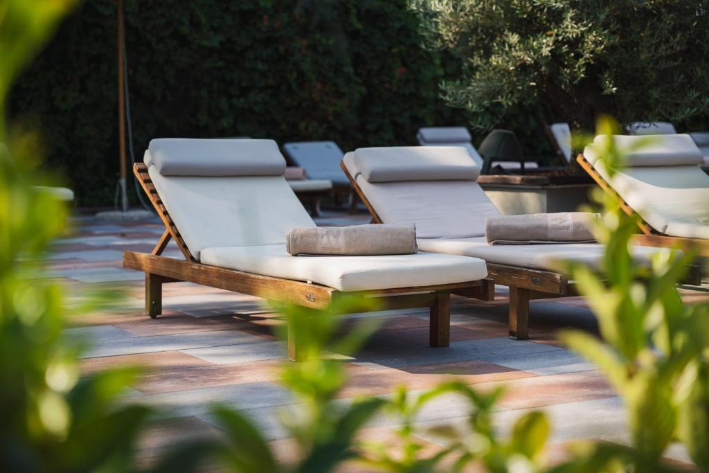 Atpūtas krēsli ar mīkstām spilveniem atrodas dārzā, ko ieskauj zaļumi un akmens segums, radot mierīgu un relaksējošu atmosfēru.