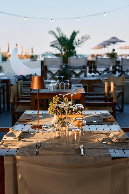 Elegantā restorāna galda kompozīcija ar ziediem un glāzēm, apgaismota ar siltu lampiņu, ar skatu uz pludmali. Ideāla atmosfēra romantiskām vakariņām.