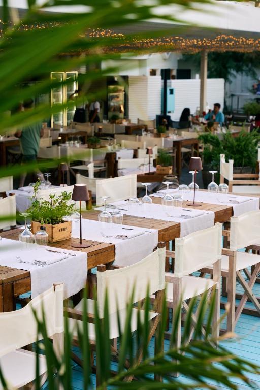 Labi iekārtots restorāna iekšpats, kur galdi ir klāti ar baltām galdautām un dekorēti ar ziediem. Apkārt ir zaļumi un cilvēki, kas bauda atmosfēru.