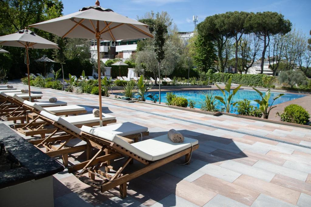 Baseina zona ar saulessargiem un guļamkrēslām, kas izvietoti blakus skaidrām ūdens virsmām un zaļām augiem. Rūpīgi kopta vide ir ideāla relaksācijai un atpūtai.