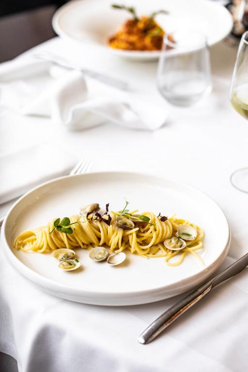 Aukstais apraksts: Eleganta pasta šķīvis ar mīdijām un garšaugiem, kas pasniegts uz baltas galdautas.