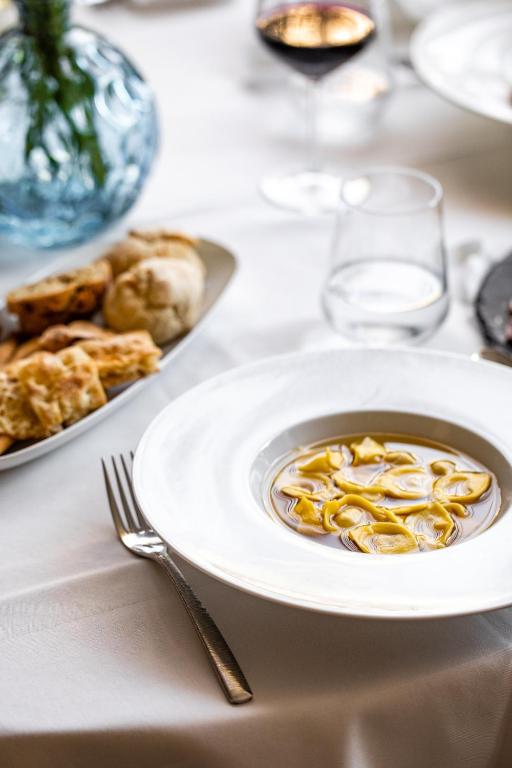 Siltā zupa ar makaroniem, pasniegta balta šķīvī, blakus maizes šķēles un vīna glāze. Elegants ēdienu noformējums.